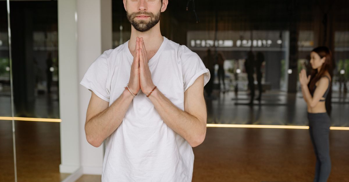 A man in a white shirt practicing yoga in a calm indoor studio, exemplifying mindfulness and relaxation.