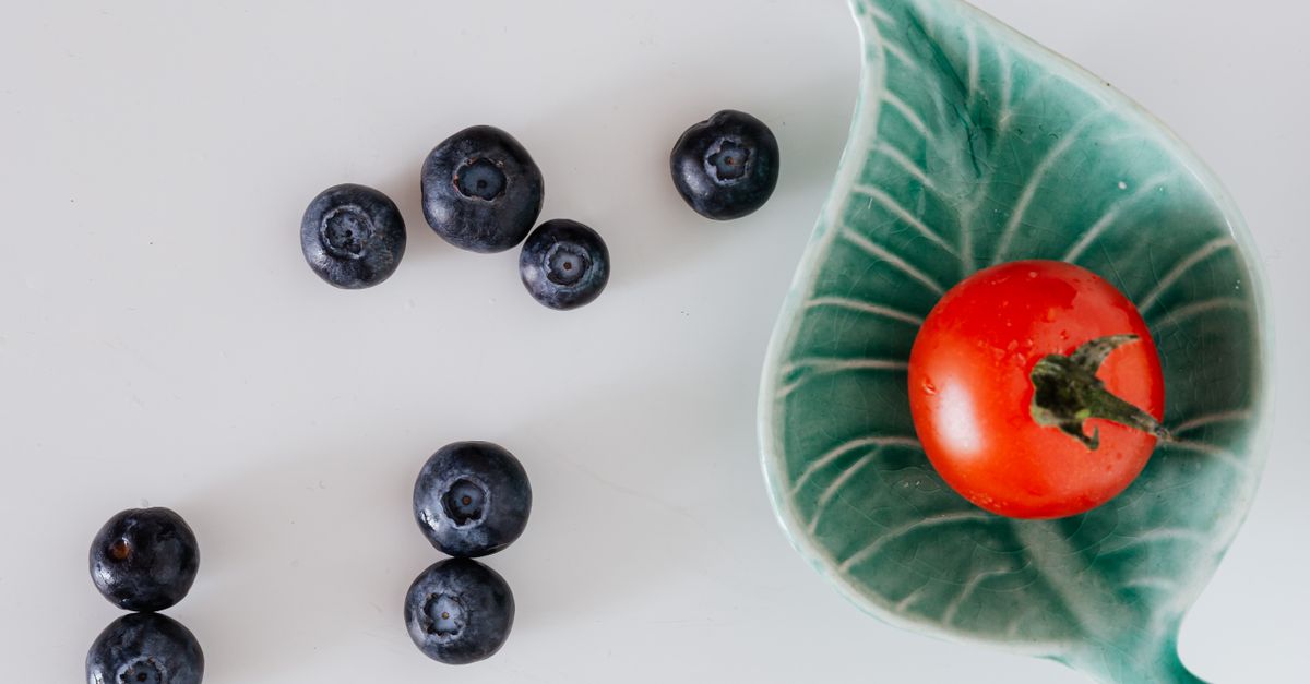 Top view of delicious blueberries near cherry tomato placed in ceramic leaf shaped saucer against gray background