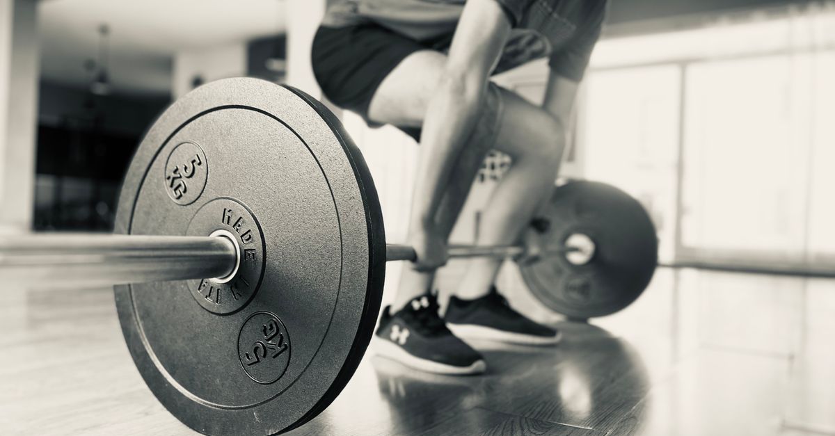 Black and white photo of a man lifting a barbell in a gym.