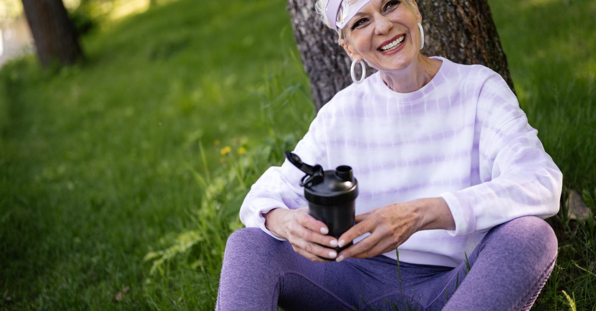 Elderly woman enjoying a sunny day outdoors, sitting on grass with a tumbler.