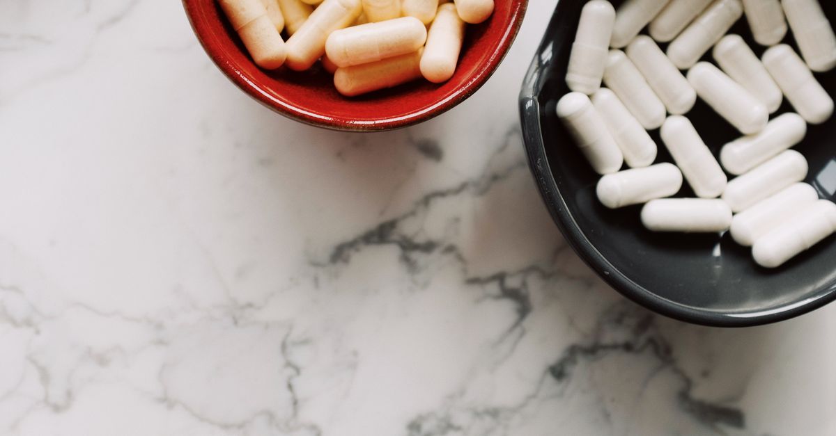 Top view of assorted capsules in bowls on a marble surface, perfect for health and wellness themes.