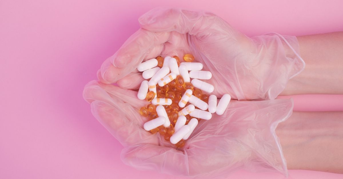 From above crop anonymous female in sterile medical gloves with handful of various medicine capsules against pink background
