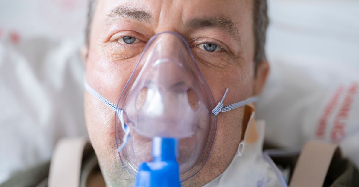 Close-up of a man in a hospital bed wearing an oxygen mask, highlighting healthcare needs.