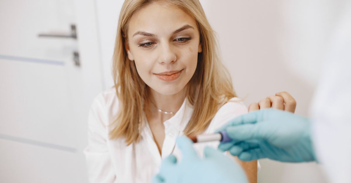 Blond woman in clinic receiving blood test with healthcare professional holding sample.