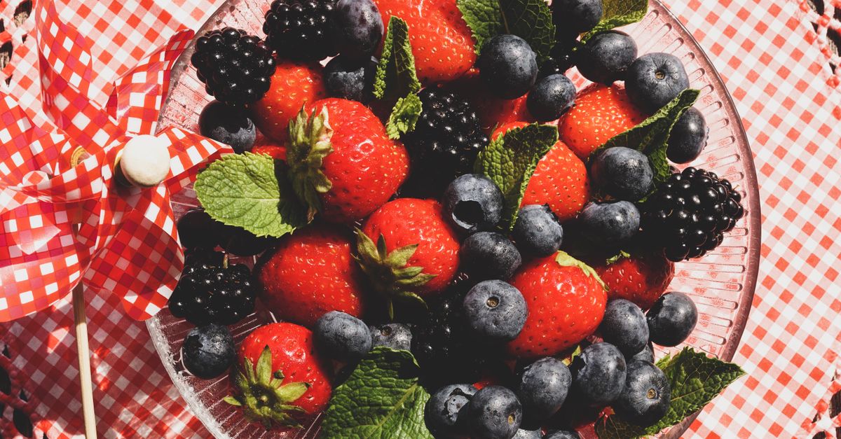 A vibrant mix of strawberries, blackberries, and blueberries with mint leaves in a glass bowl.