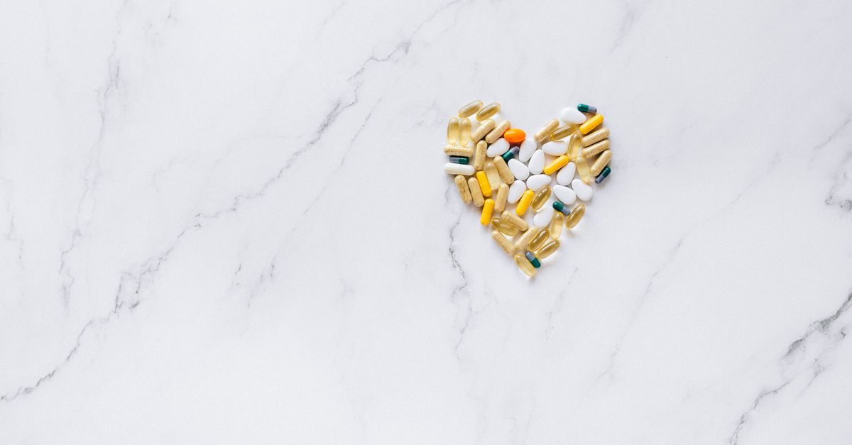 Colorful pills arranged in a heart shape on a marble surface, symbolizing healthcare and well-being.
