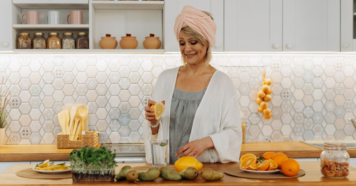 Smiling woman squeezing orange in a modern kitchen setting, emphasizing citrus freshness and healthy lifestyle.