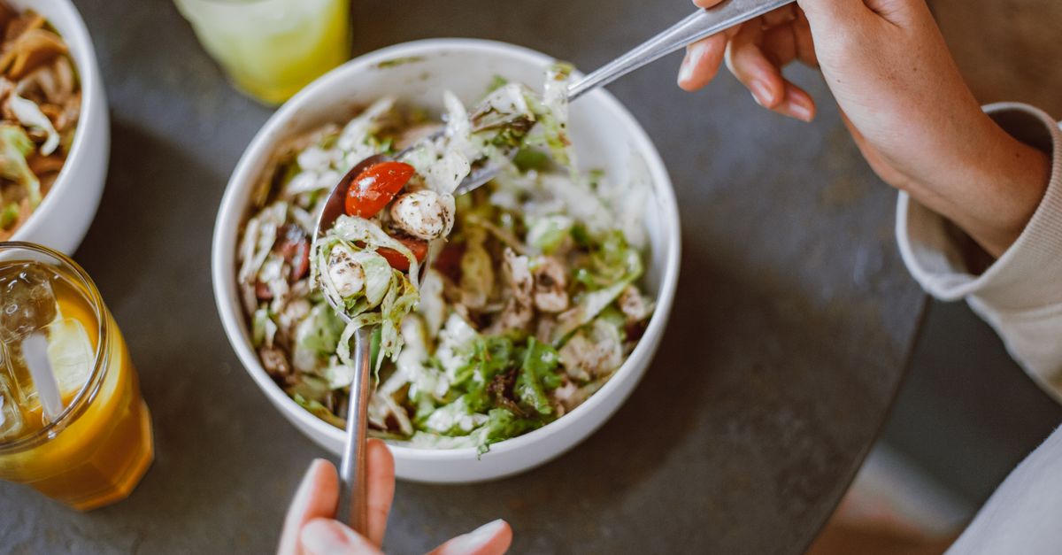 A person enjoying a fresh salad with cherry tomatoes and greens indoors.
