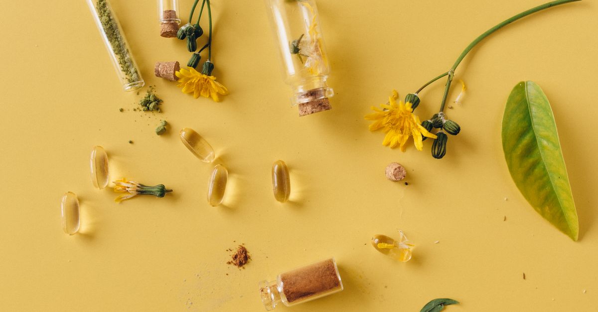 A flat lay of glass bottles, capsules, and flowers on a vibrant yellow surface, representing natural remedies.