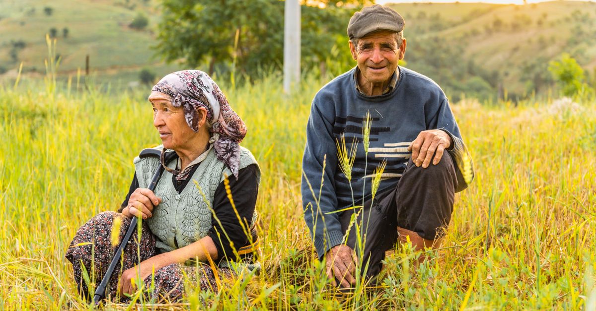 Senior farmers sitting in a grassy field, smiling and enjoying a peaceful day outside.
