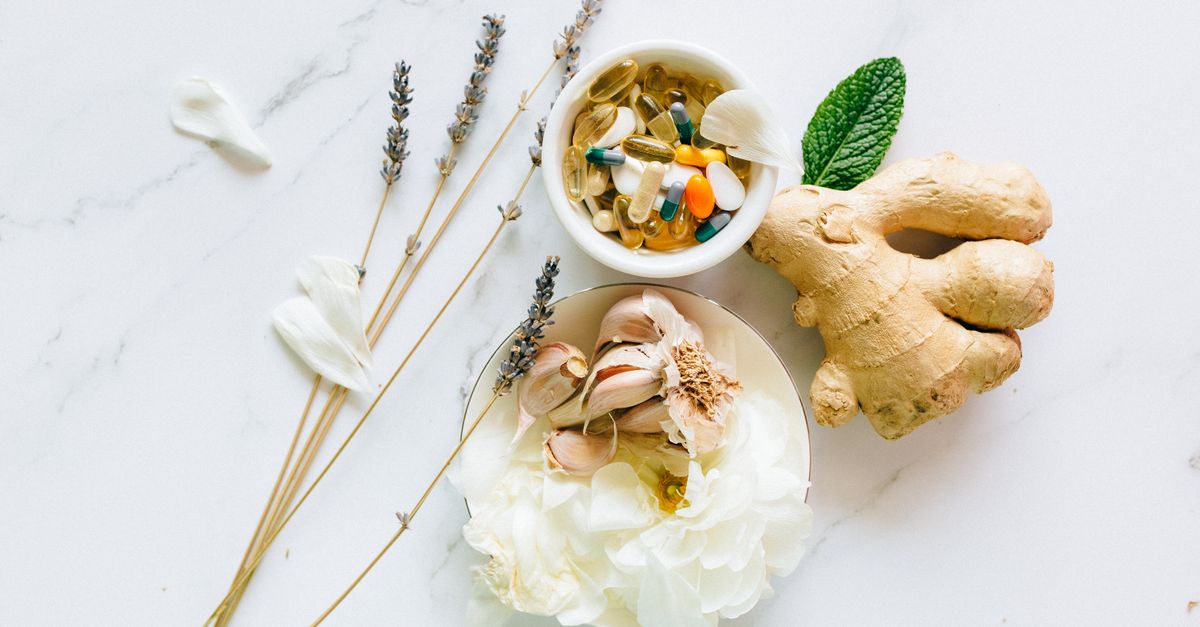 Flat lay of ginger, garlic, flowers, and supplements for holistic health.