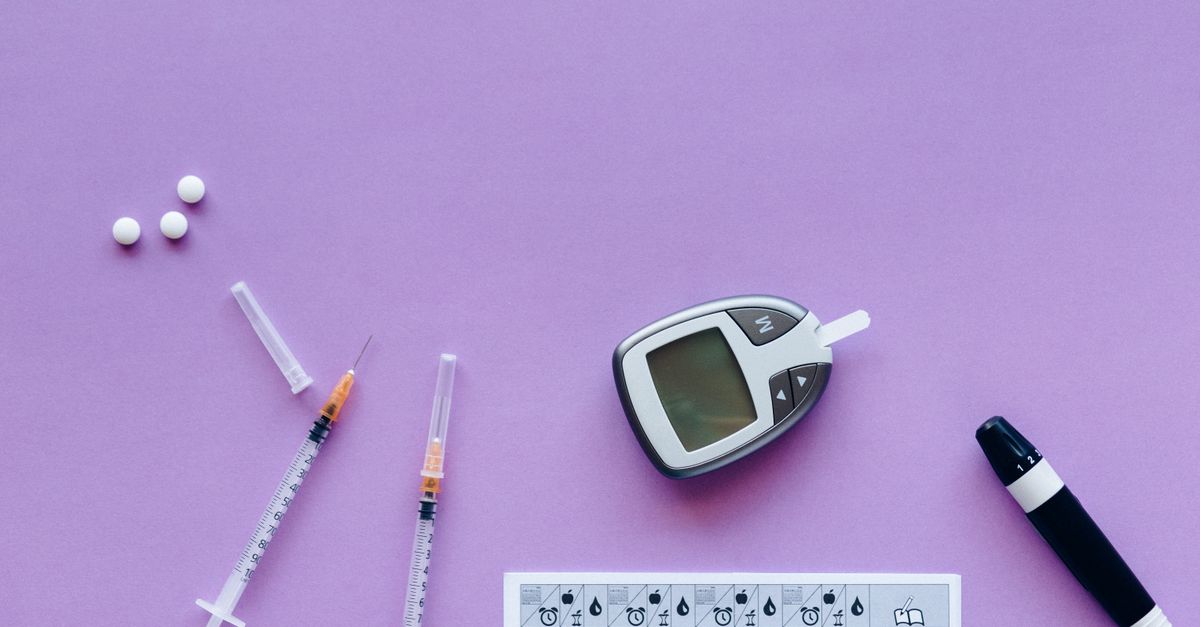 Flat lay of diabetes management tools including glucometer, syringes, and pills on purple background.