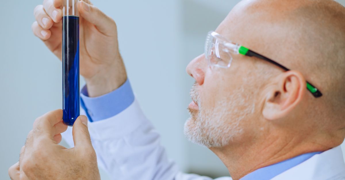Scientist in lab coat examines a blue liquid in a test tube, showcasing focus and concentration.