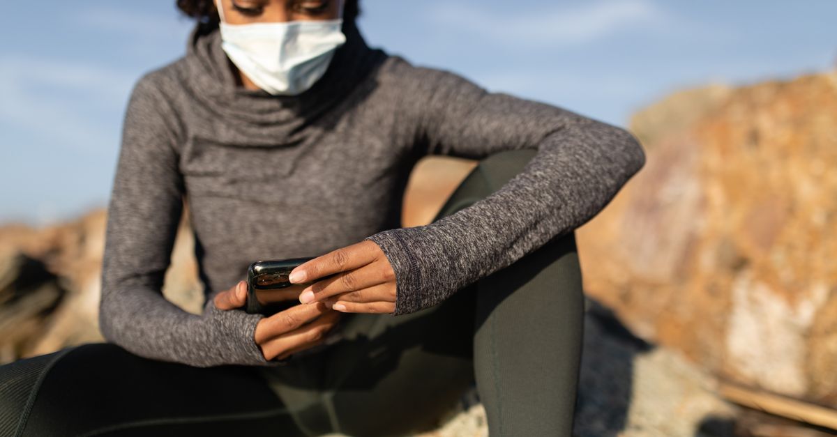 Focused woman wearing a face mask and using a smartphone while sitting outdoors.