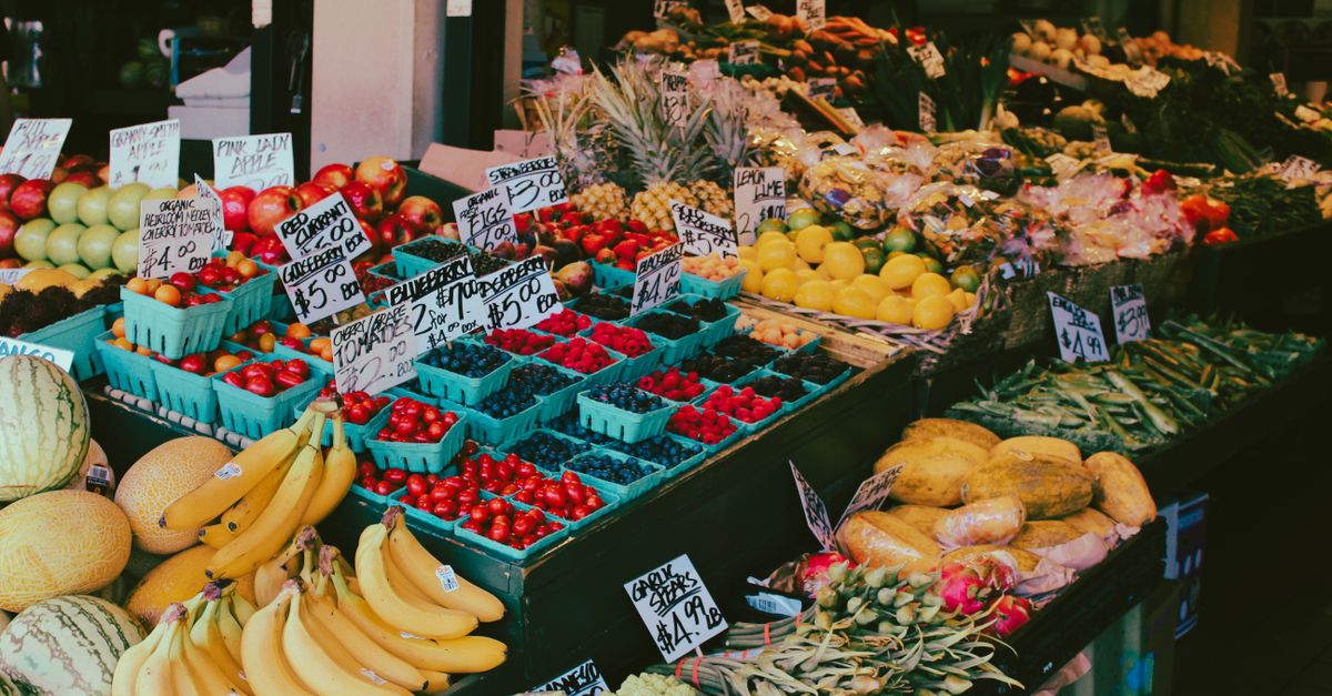 Colorful fruit and vegetable market stall displaying a variety of fresh produce with visible price tags.
