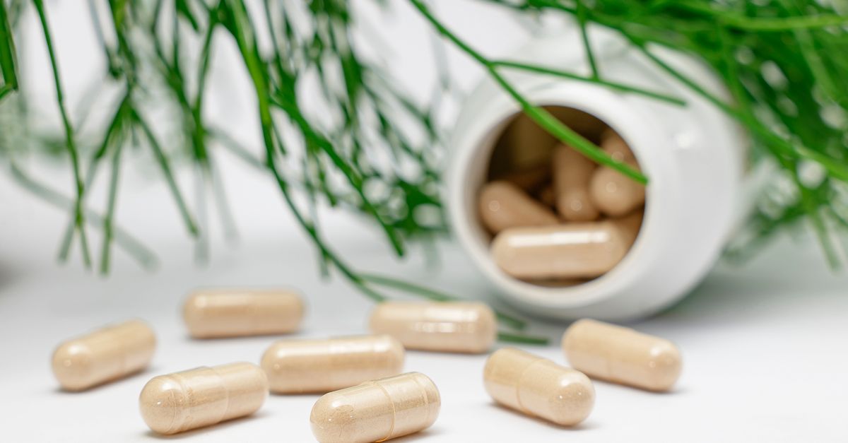 Close-up of herbal capsules spilling from a bottle with green plants in the background.