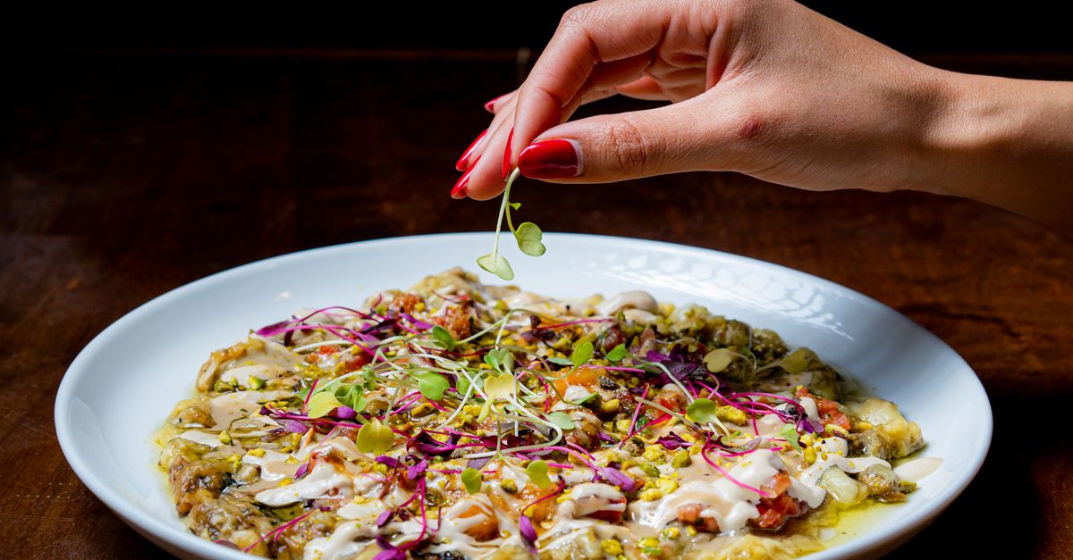 A hand delicately garnishing a gourmet dish with fresh herbs, enhancing culinary presentation.