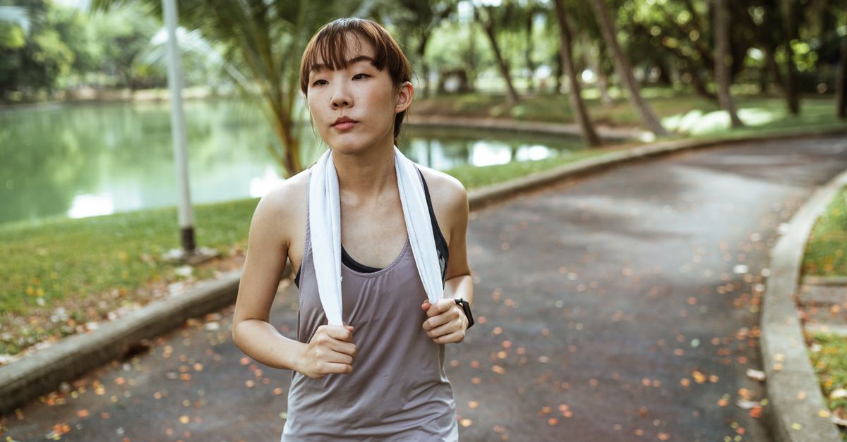 Serious ethnic female athlete wearing sportswear and smart watch looking away while jogging alone in park at daytime in summer day