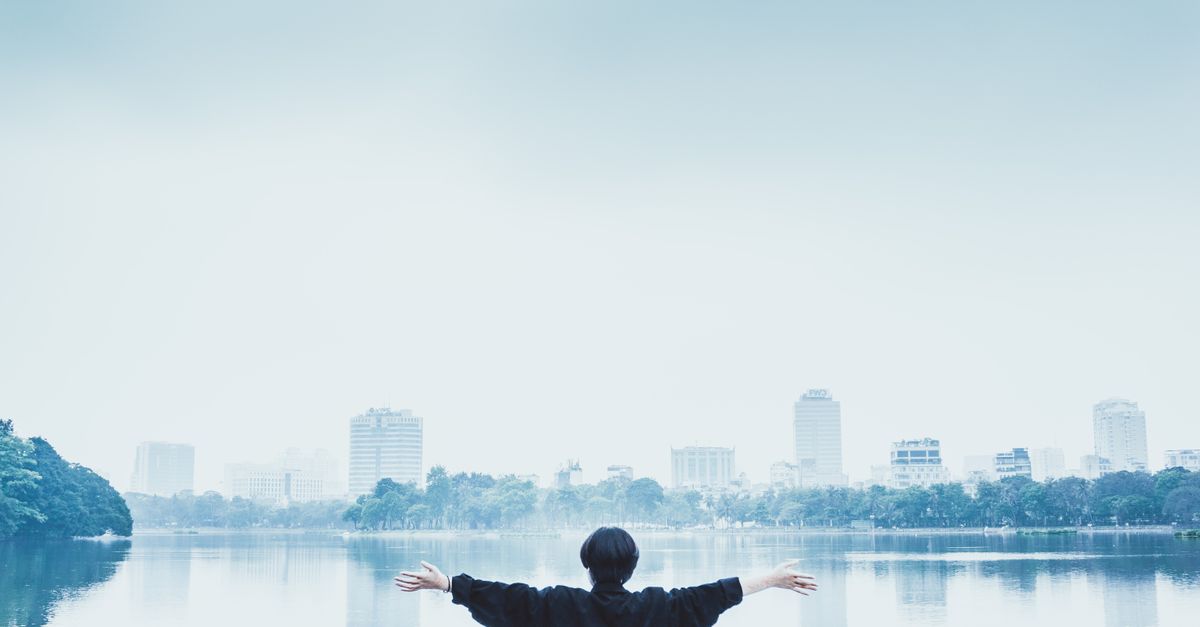 A person standing with arms spread wide embracing a serene cityscape by the lake.