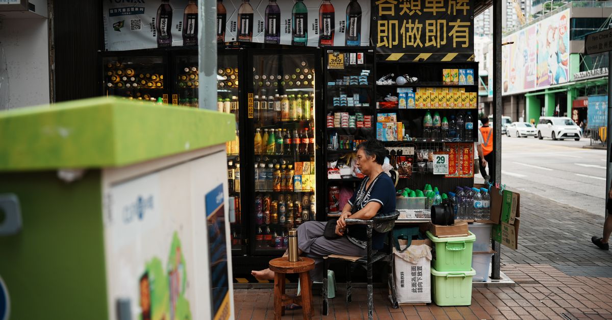 A local vendor sits at a bustling street kiosk selling drinks and snacks in an urban environment.