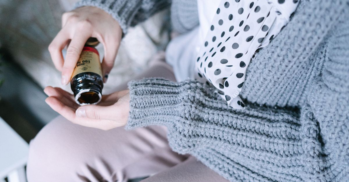 Close-up of a woman in cozy clothing holding a medicine bottle in her hands.