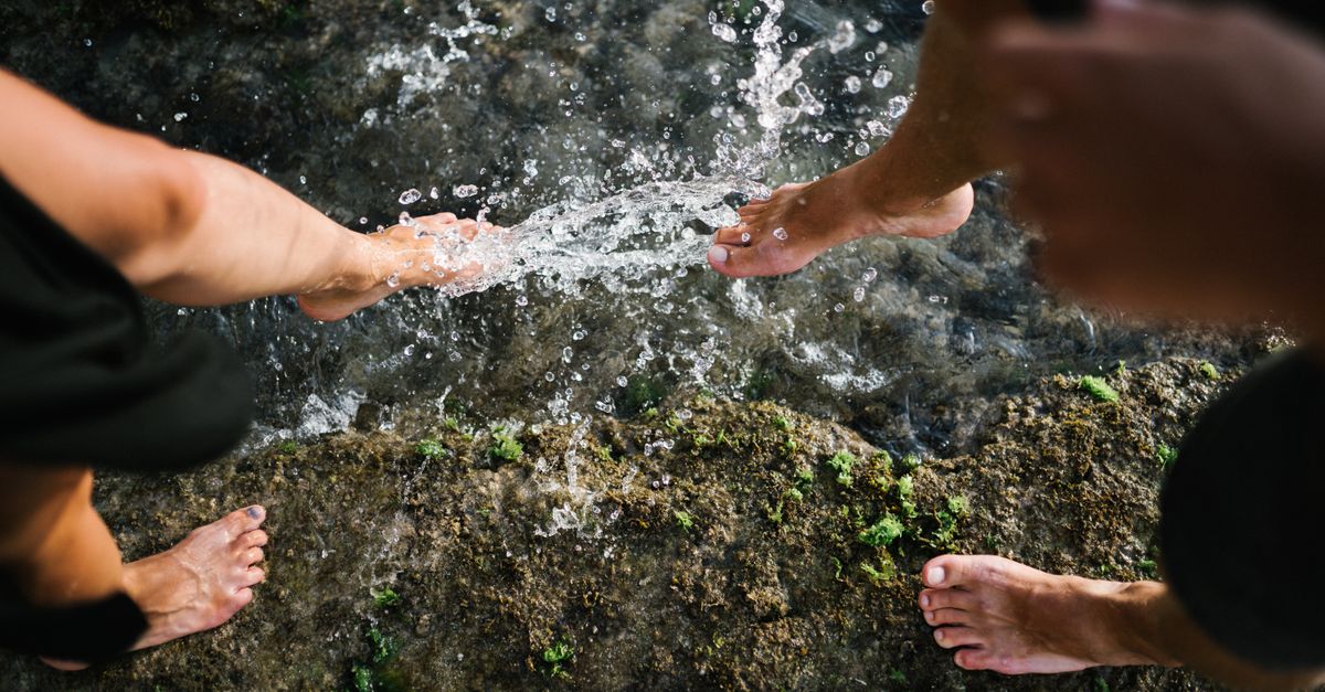 Close-up of bare feet splashing water on rocks outdoors, showcasing playful interaction with nature.