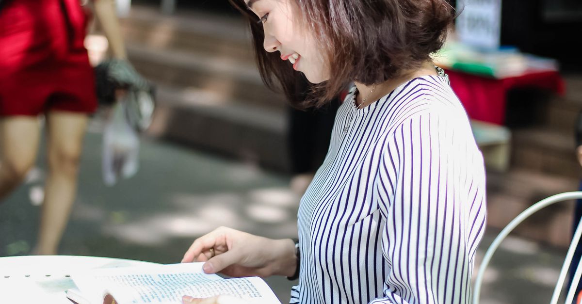 A woman reading a book at an outdoor setting, captured in natural daylight.