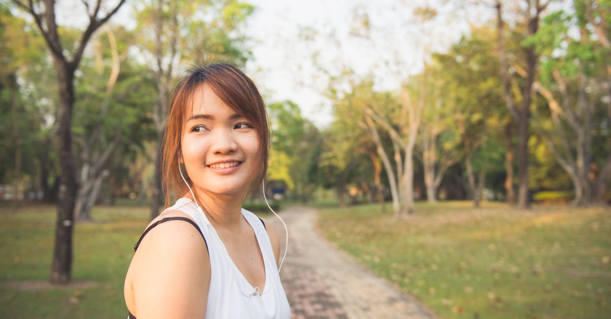 Smiling young woman jogging with earphones in a sunlit park.
