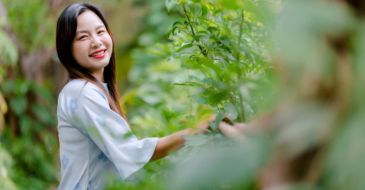 Happy woman in blue kimono smiling amidst lush greenery outdoors.