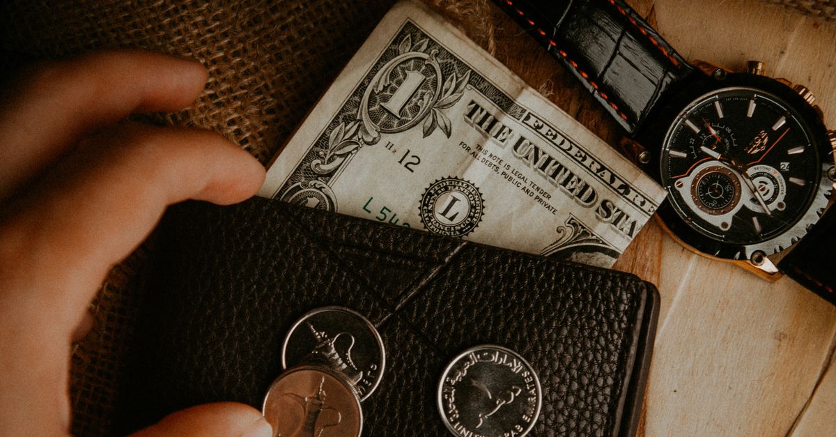 A detailed look at a wallet with money and a watch on a wooden surface.