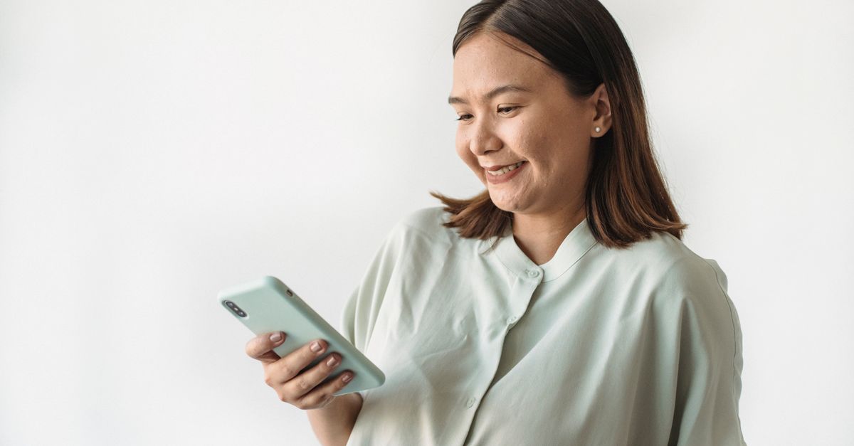 Happy woman in casual attire smiling while using her smartphone against a white background.