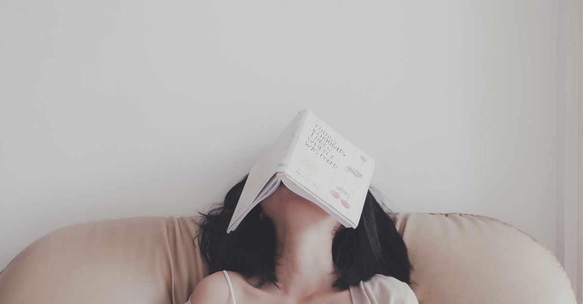 A woman relaxes indoors with an open book resting on her face, enjoying a tranquil moment.