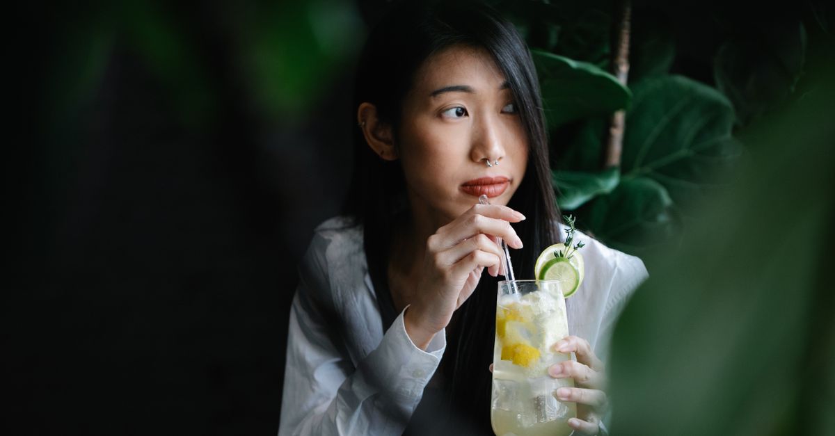 Portrait of a woman sipping lemonade through straw in a serene setting.