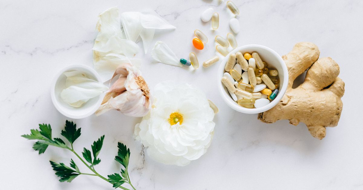 Top view of herbal medicine and supplements with ginger, flower, and capsules on a white background.