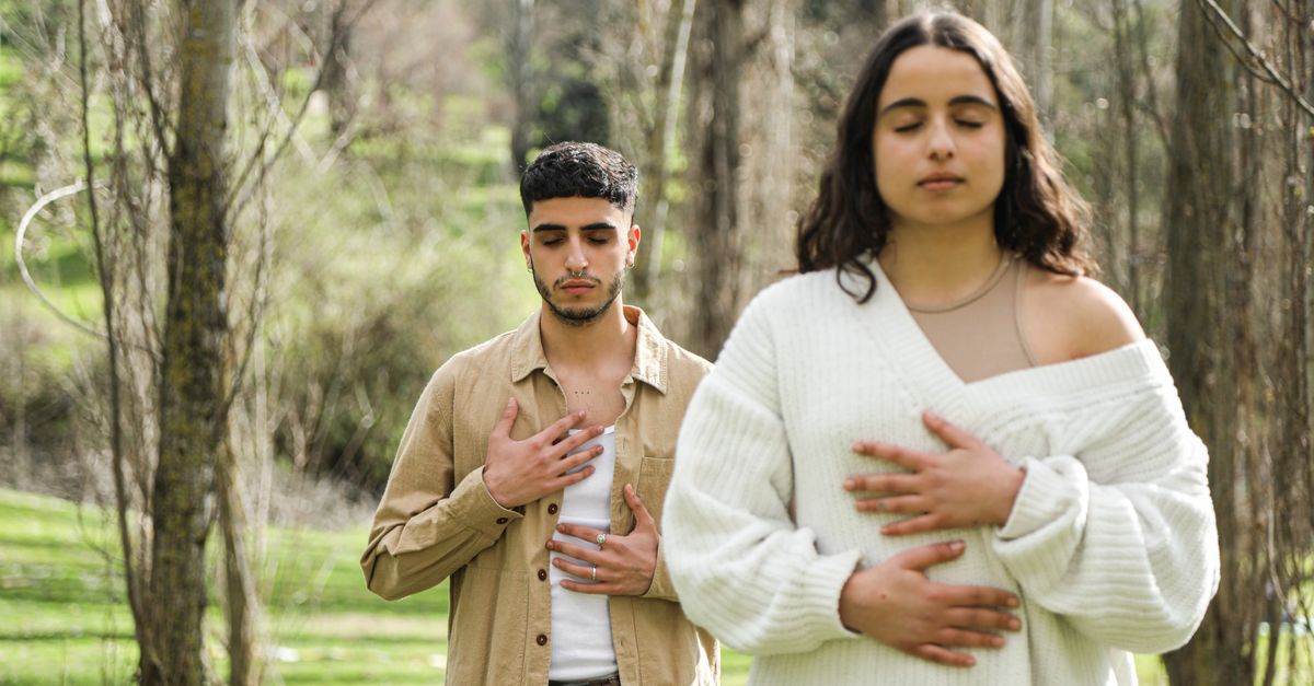 A man and woman meditating with closed eyes, embodying peace and relaxation in a forest.