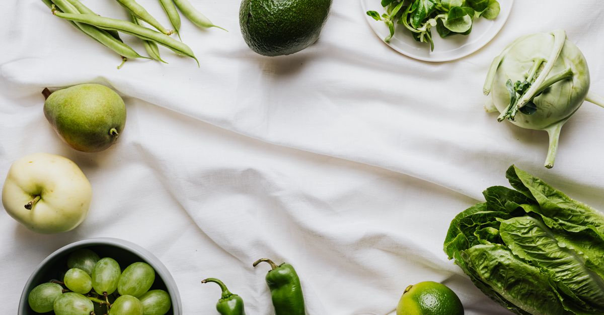 Top view of assorted fresh green vegetables and fruits arranged on a white background for healthy eating concept.