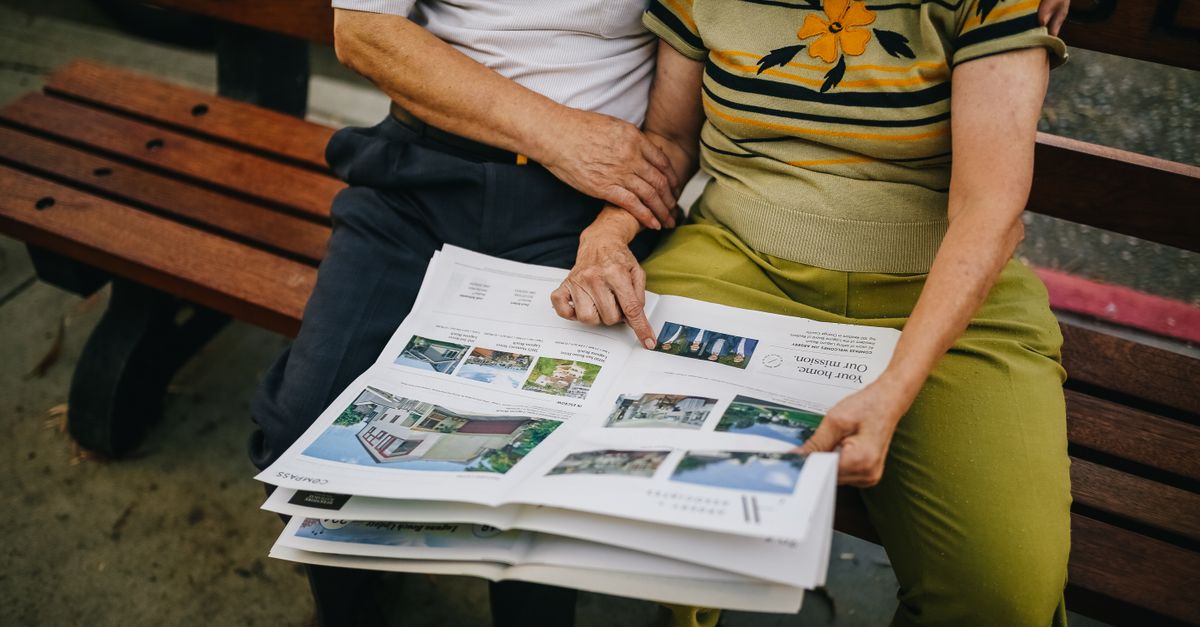 Elderly couple sitting outdoors, reading and embracing on a park bench.