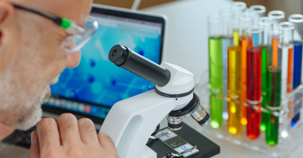 Scientist using microscope with colorful test tubes in a modern laboratory setting.