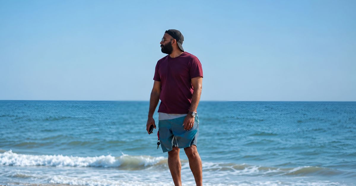 A man relaxes on a sandy beach under a clear sky, enjoying the summer day by the ocean.