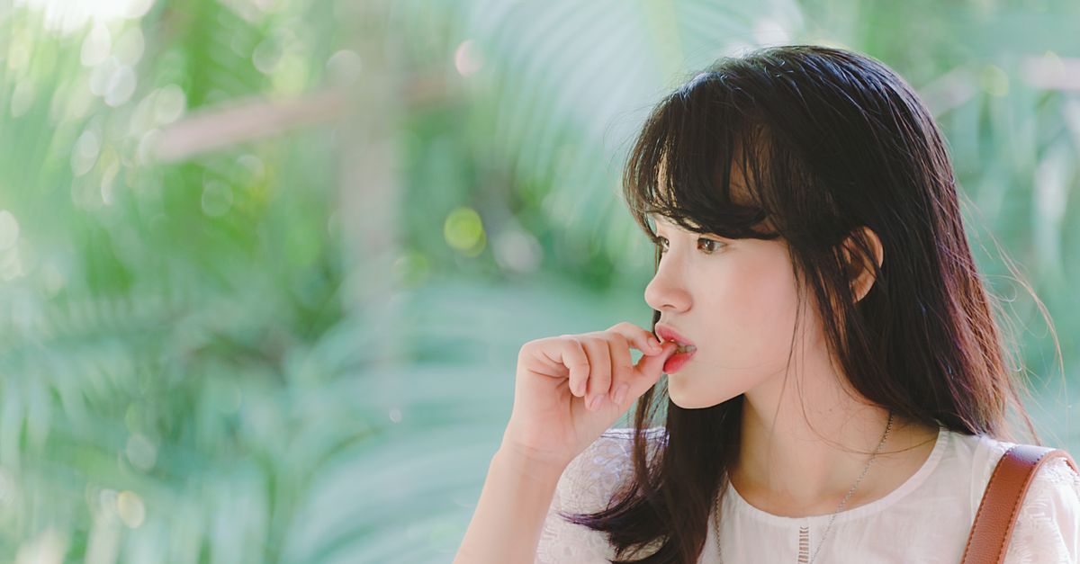 A young woman deep in thought surrounded by vibrant green foliage on a sunny day.