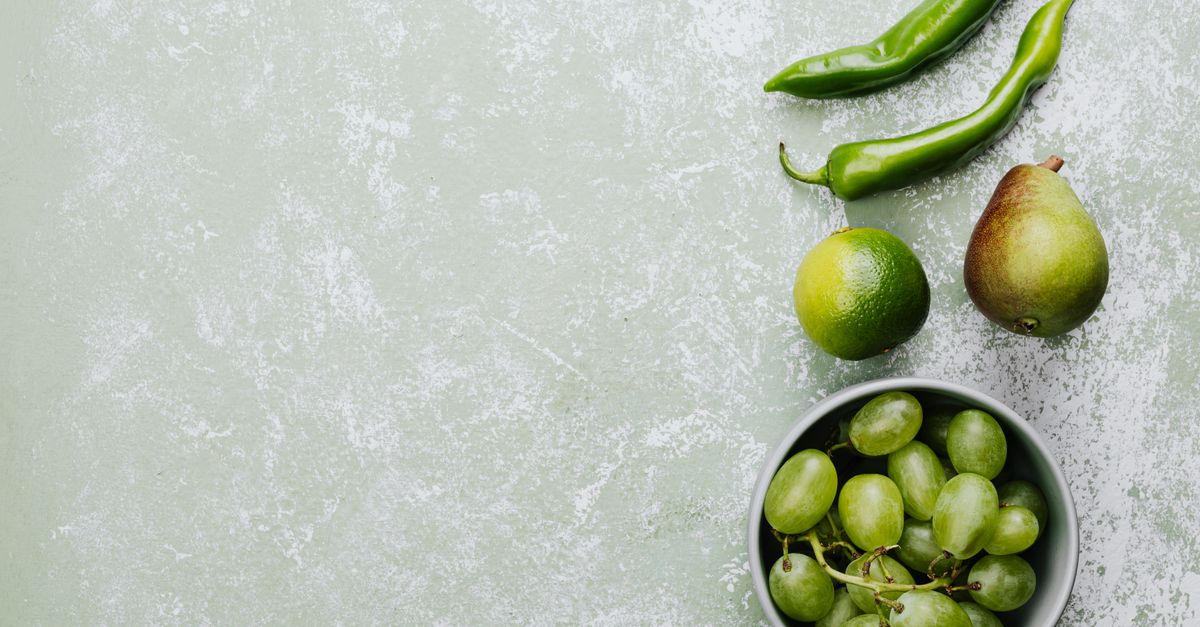 A flat lay of green grapes, pepper, lime, and pear with ample copy space on a textured backdrop.