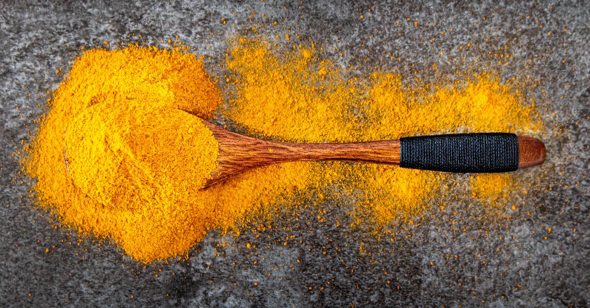 Vibrant turmeric powder spread with a wooden spoon for cooking inspiration.