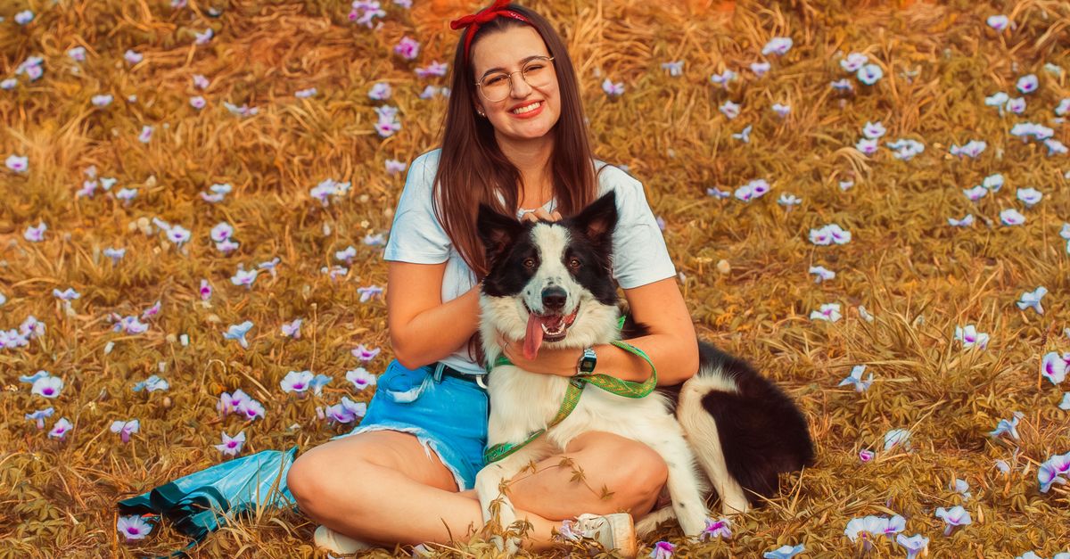 Woman and border collie enjoying a sunny day in a flower-filled field.