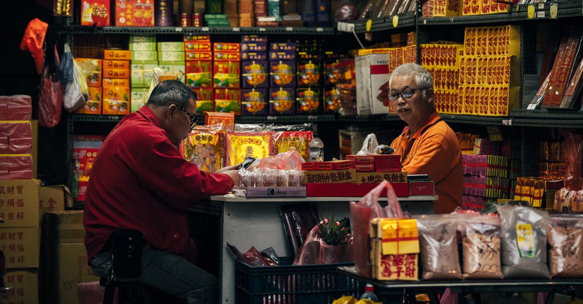 Two elderly men managing a traditional Asian market store indoors, surrounded by colorful products.