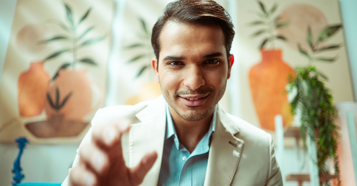 Confident businessman reaching towards camera in modern casual office setting.