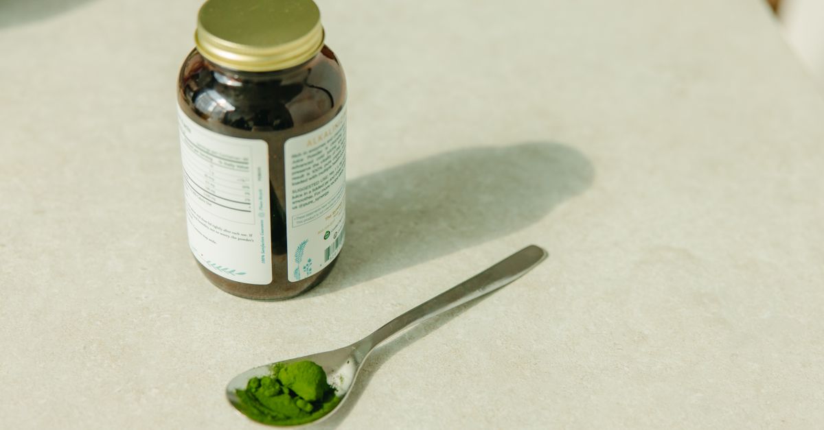 Close-up of a jar and a spoon with green powder, ideal for healthcare and wellness themes.