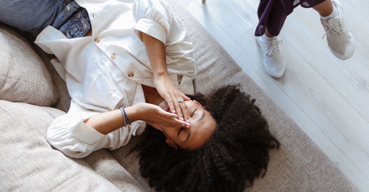 A woman with afro hair lies relaxed with eyes closed on a sofa indoors.