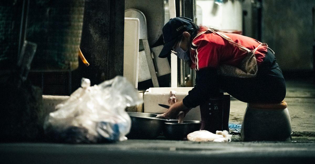 A woman wearing a mask is working on the street at night, emphasizing urban life.