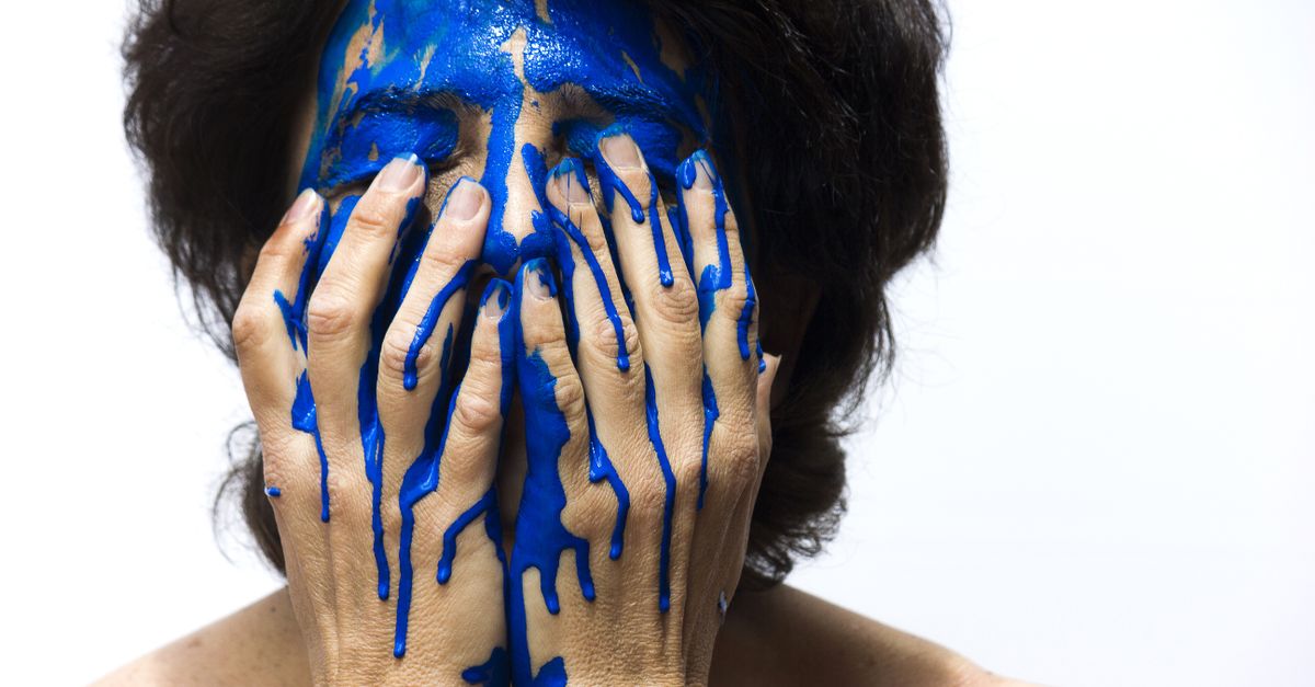 A striking artistic portrait of a woman covered in blue paint, expressing emotion and creativity.