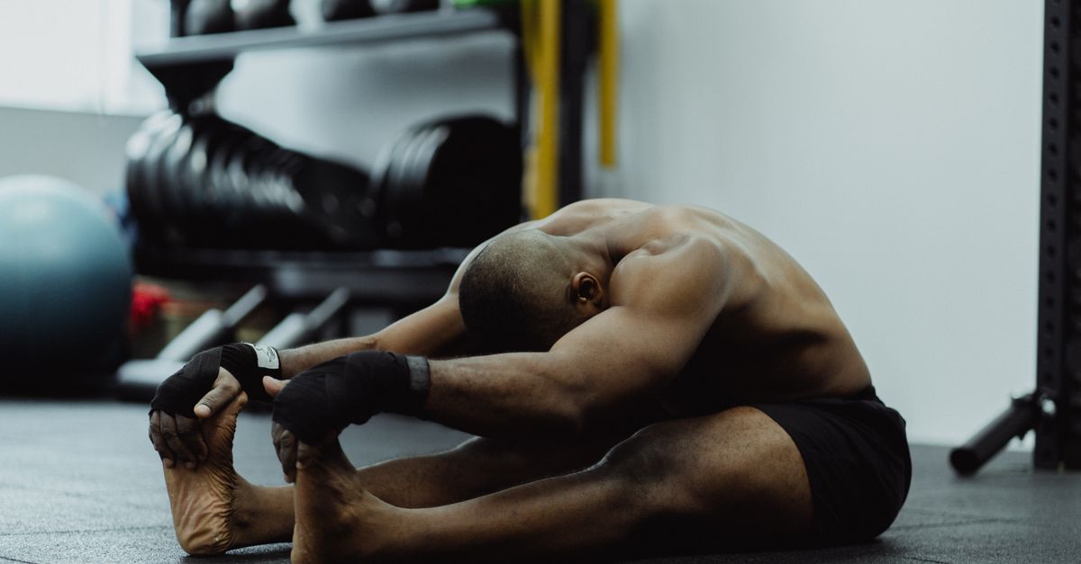 Man doing seated stretch in gym, emphasizing fitness and flexibility training.